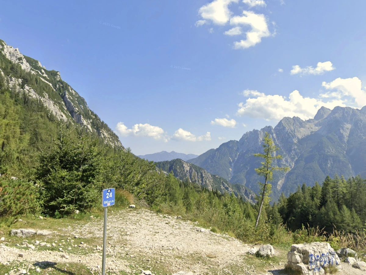 View of the Julian Alps from the Vršič Pass with green trees and gravel road