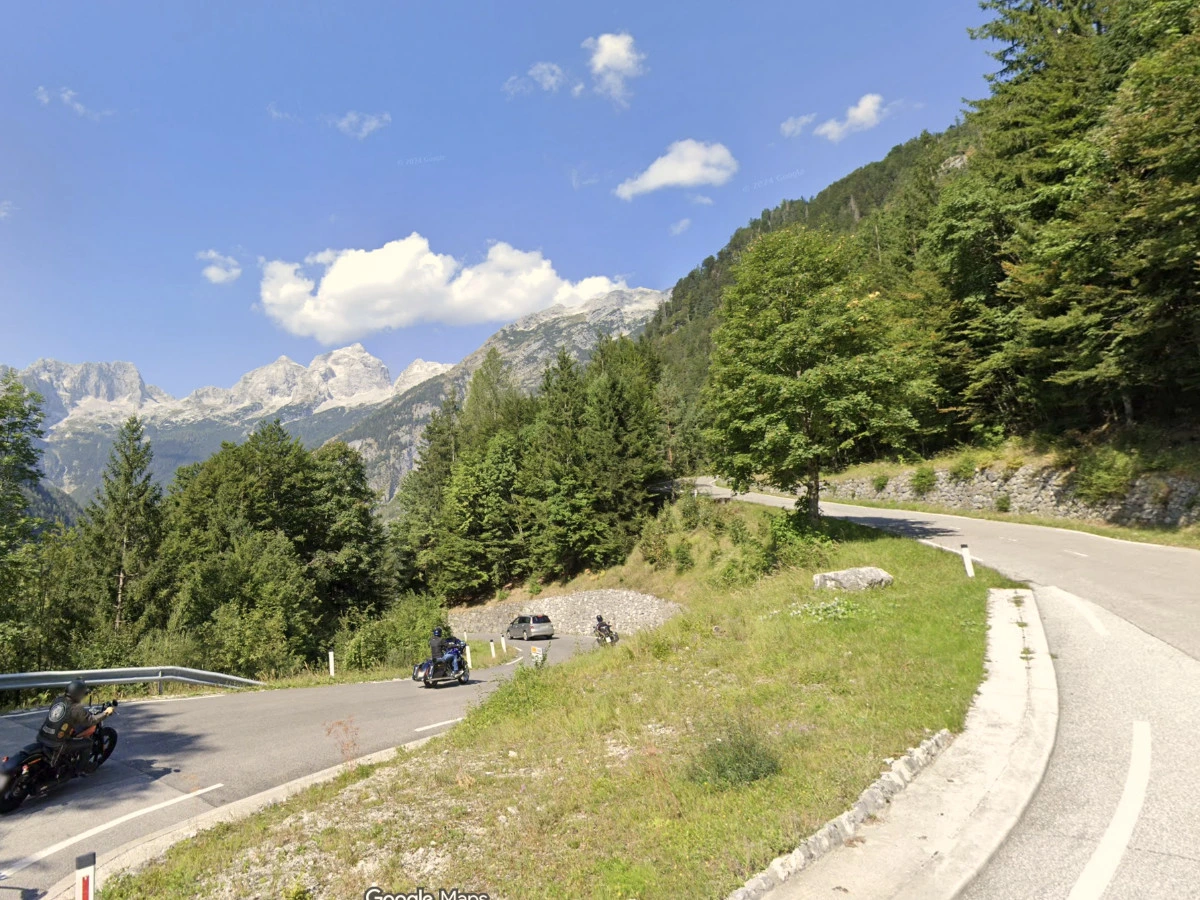 Vršič pass hairpin road with green trees and mountains in the distance