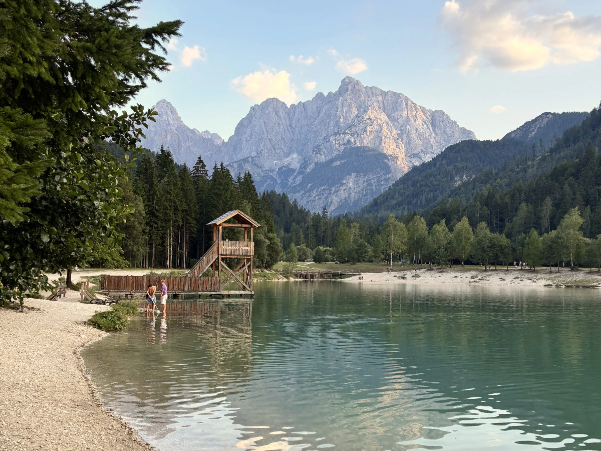 Lake Jasna with a wooden tower, surrounded bz trees and gravel with mountains in the distance