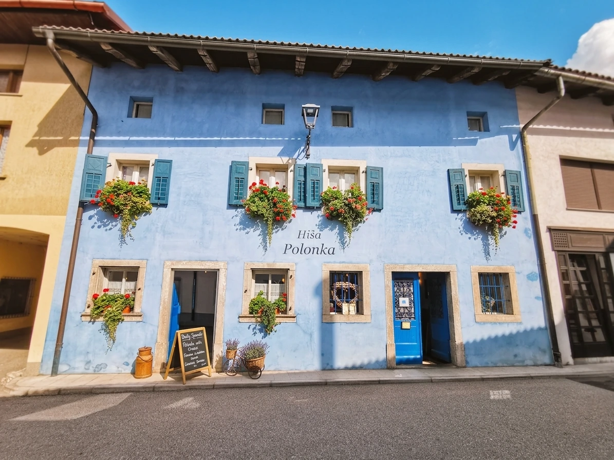 Outside of restaurant Hiša Polonka with a blue facade and windows with window shutters and flowers
