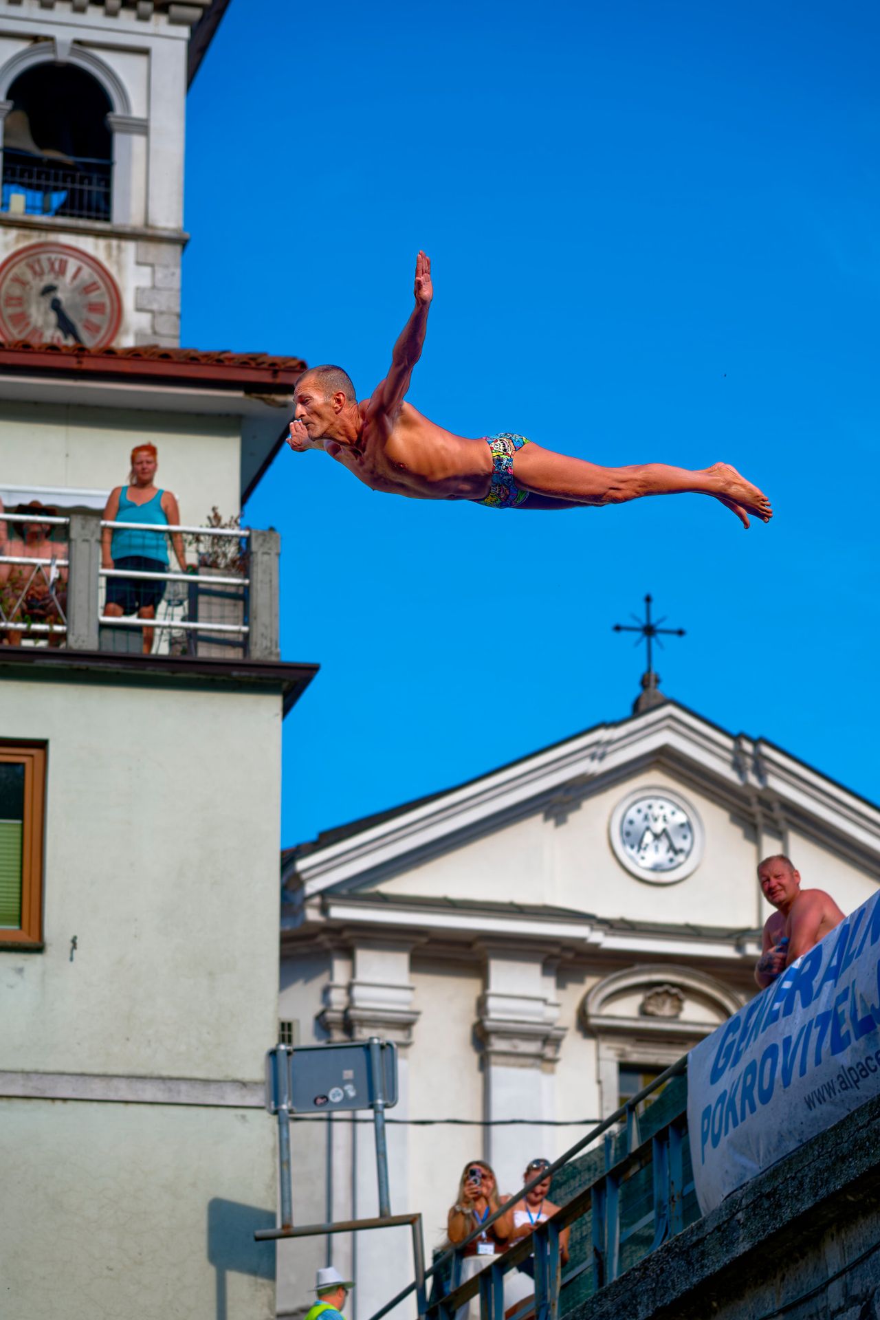 Diver jumping off the bridge with local buildings in the back.