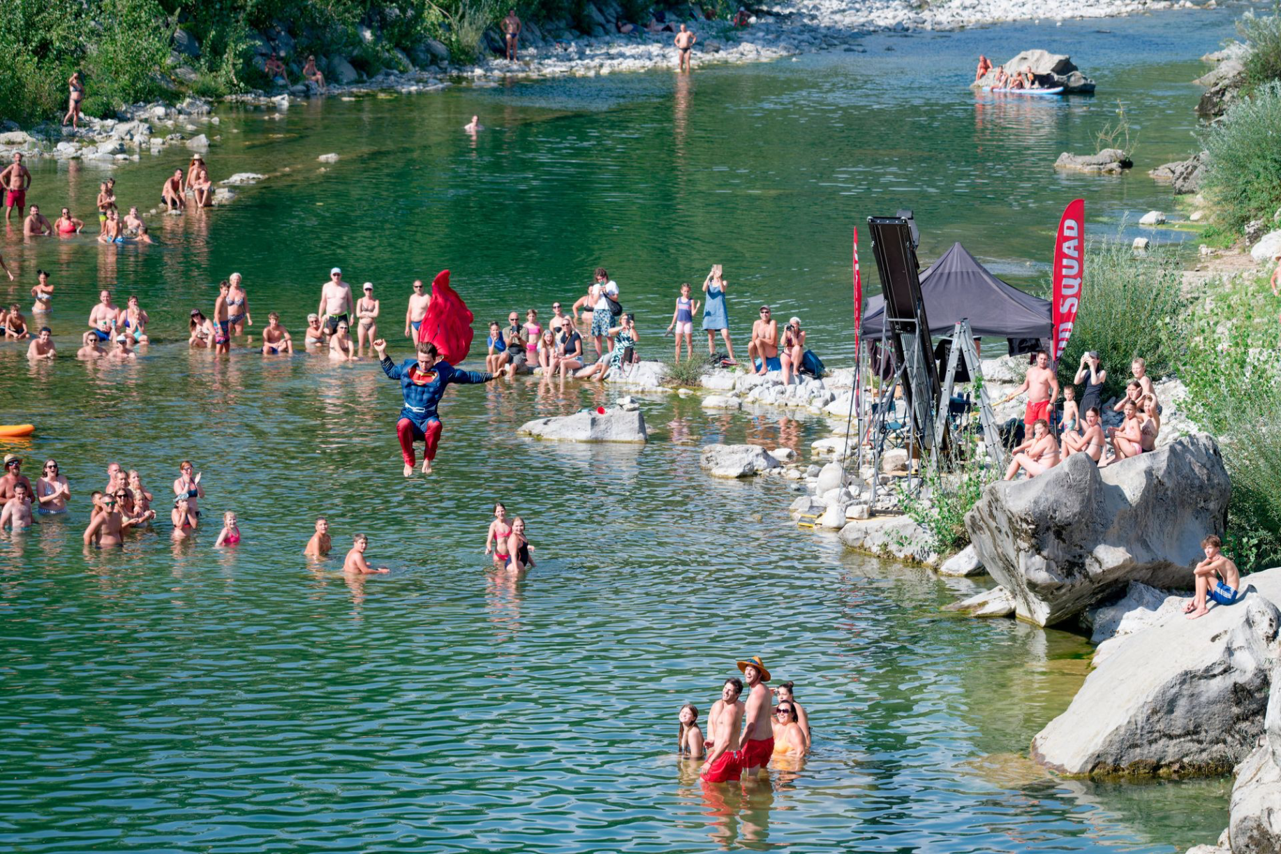 Audience sat by river Soca watching a diver, dive in a superman costume